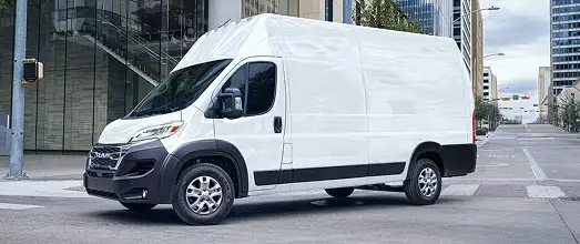 White RAM ProMaster high-roof cargo van parked on a city street beside a glass building