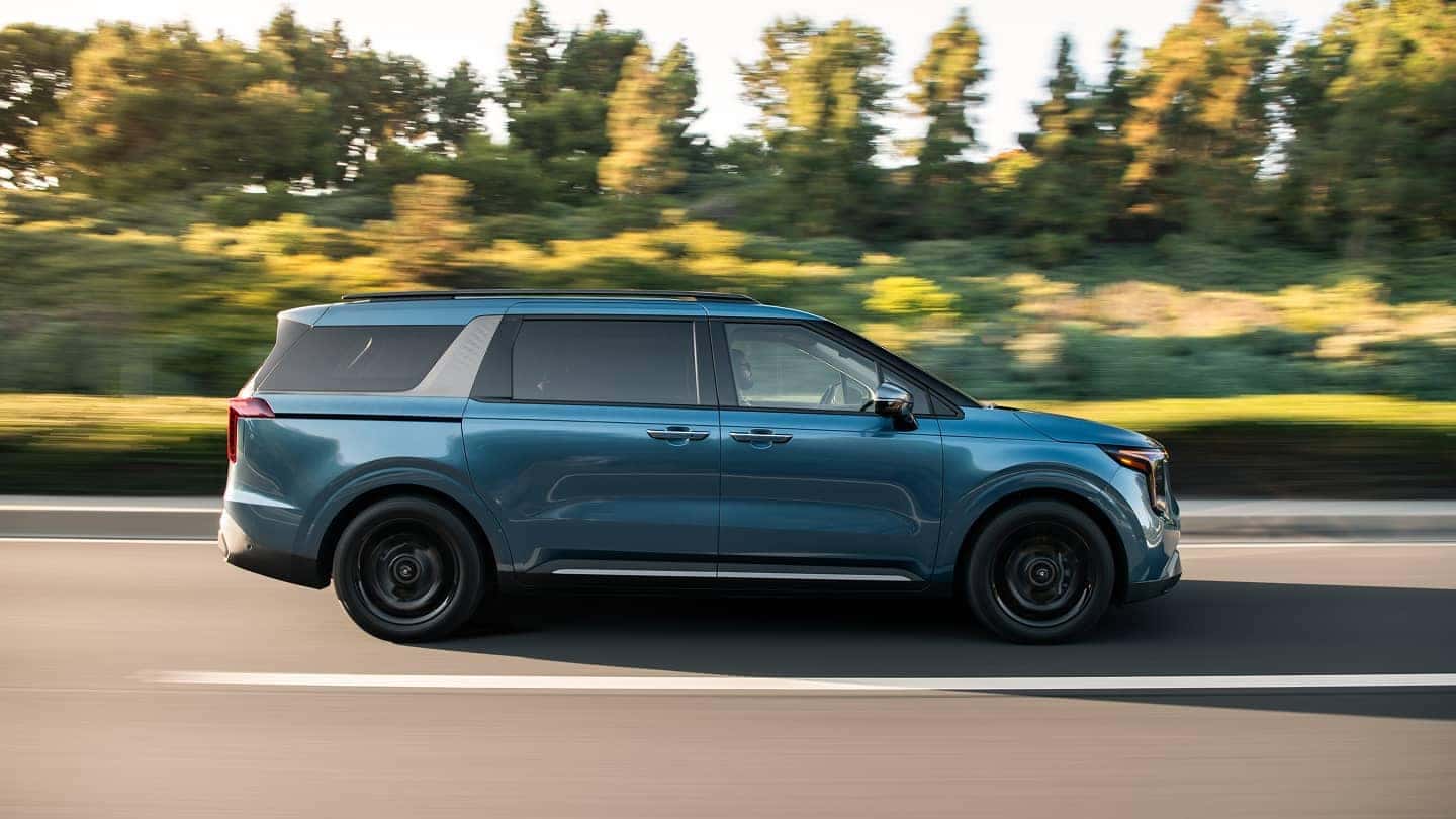 2025 Kia Carnival action shot along tree lined road
