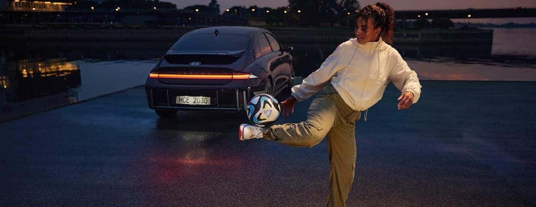 Women Playing with Soccer Football Behind Hyundai Sedan