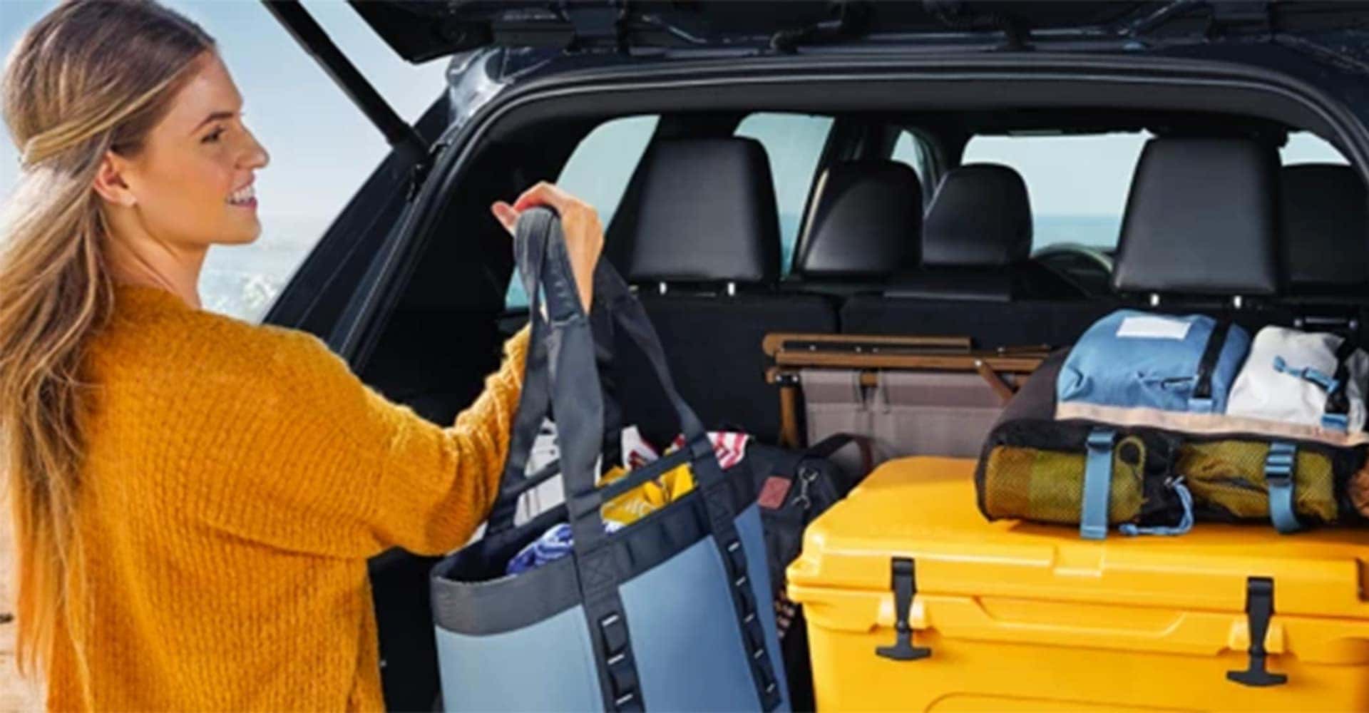 Trunk shot of Grand Highlander 2025, woman taking camping gear out of trunk