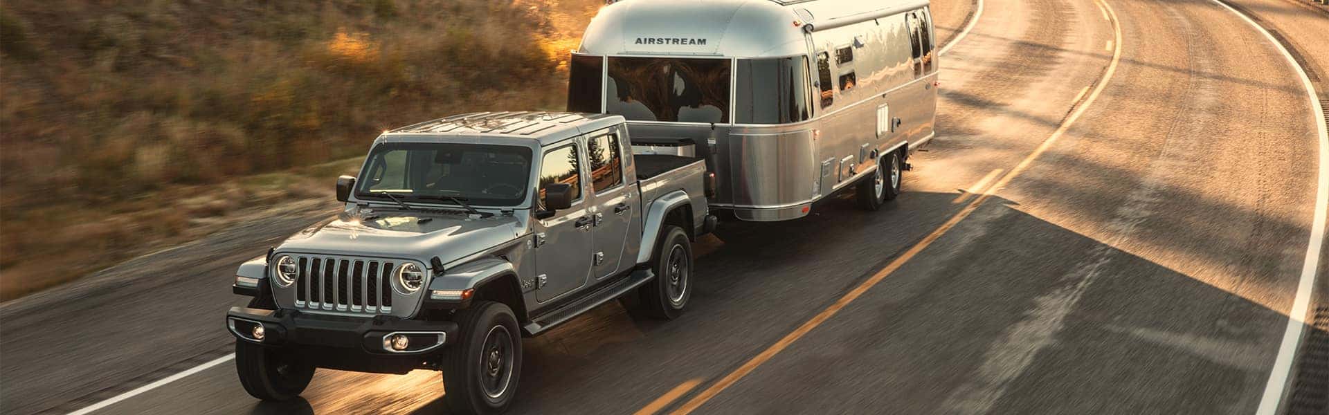 Benefits of Changing Your Chrysler Dodge Jeep Ram’s Oil at Winner's Circle CDJR in Hampton VA | Silver 2020 Jeep Gladiator Pulling Trailer While Driving on Country Road